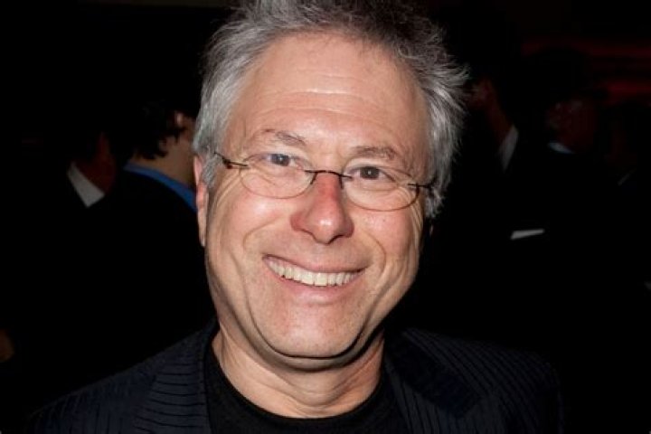 Alan Menken in a black and silver suit in front of a purple backdrop at the live-action 'Aladdin' premiere