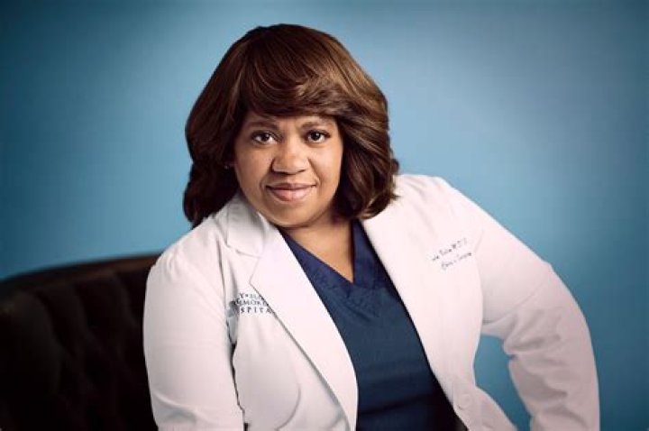 Chandra Wilson as Miranda Bailey on 'Grey's Anatomy' sits smiling in a white coat.