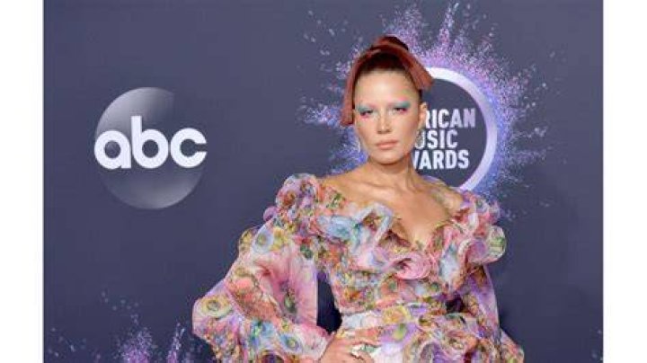 Halsey holds a microphone and sits on a couch at an event.