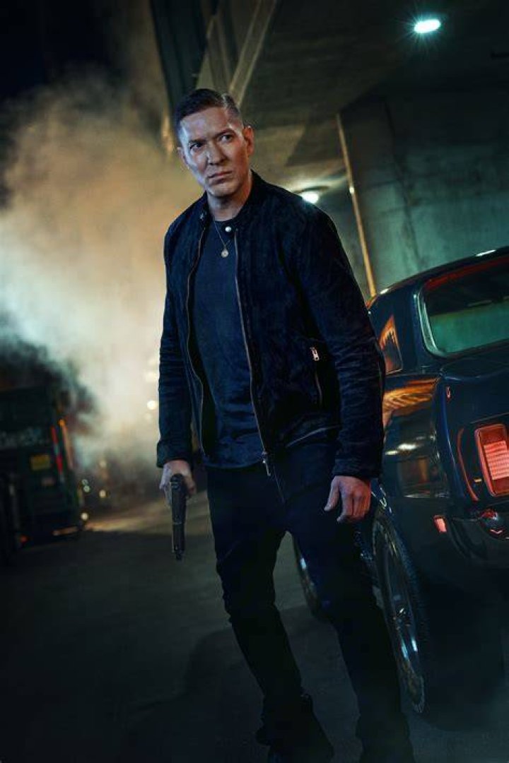 Joseph Sikora as Tommy Egan in 'Power Book IV: Force' wearing a leather jacket and gold chain while smirking