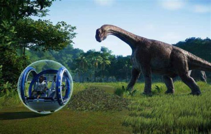 Jurassic World Evolution 2 Gyrosphere inside herbivore enclosure. There is a ranger team in the middle of the image and a handful of herbivorous dinosaurs.