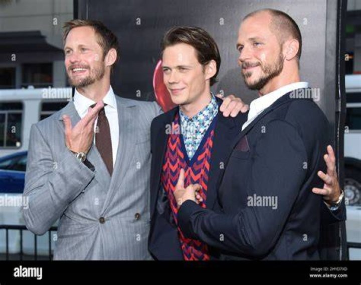(L-R) Gustaf, Bill, and Alexander Skarsgard smiling in front of a black background