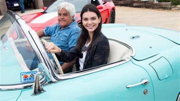 (L-R) Jay Leno and Kendall Jenner smiling sitting in a blue convertible