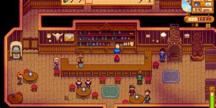Stardew Valley, Stardrop Saloon. The player is stood at the till on the long wooden bar. The bartender, Gus, is stood behind the bar cleaning a glass.